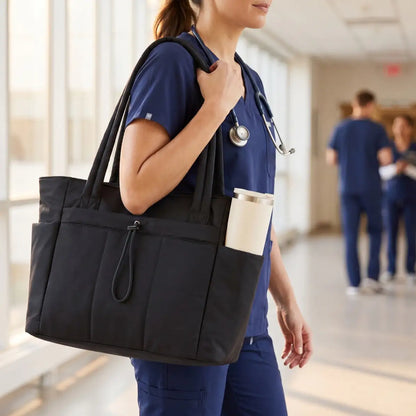 A nurse in navy scrubs carrying the Everyday Laptop Tote with an insulated tumbler in the side pocket