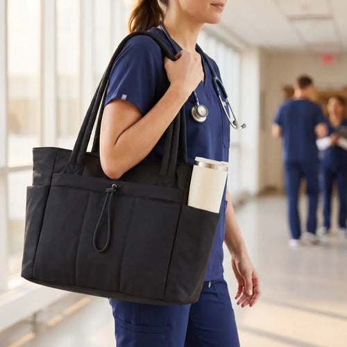 A nurse in navy scrubs carrying the Everyday Laptop Tote with an insulated tumbler in the side pocket
